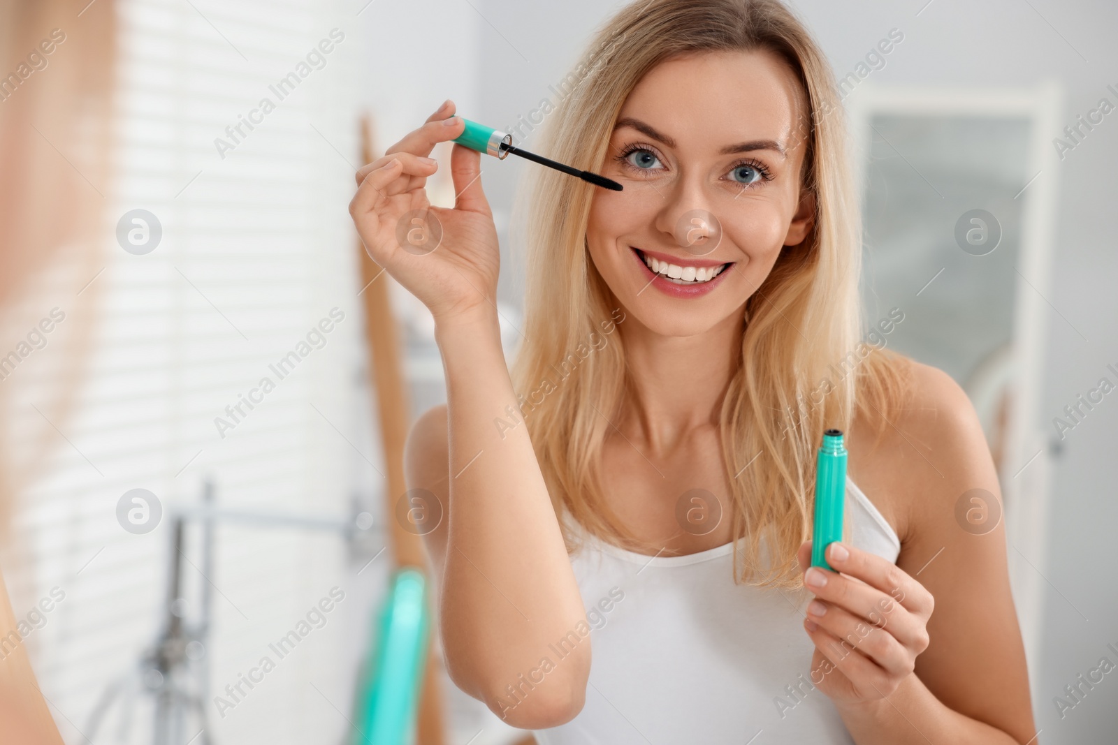 Photo of Beautiful woman applying mascara near mirror in bathroom