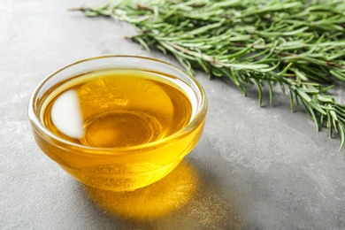 Photo of Bowl with fresh rosemary oil on grey table