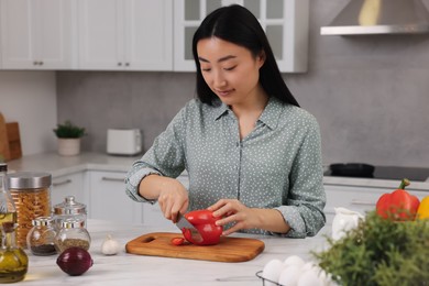 Photo of Cooking process. Beautiful woman cutting bell pepper at white countertop in kitchen