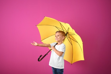 Little boy with yellow umbrella on color background