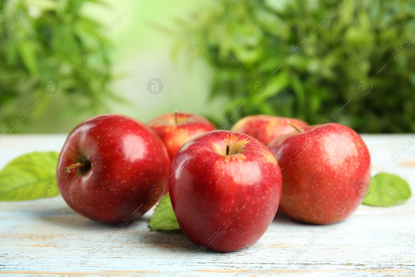 Photo of Ripe juicy red apples on white wooden table against blurred background. Space for text