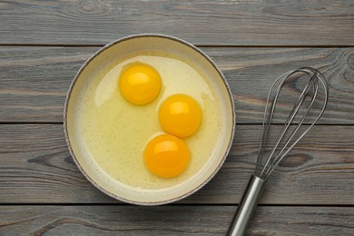 Photo of Whisk near bowl with eggs on wooden table, flat lay