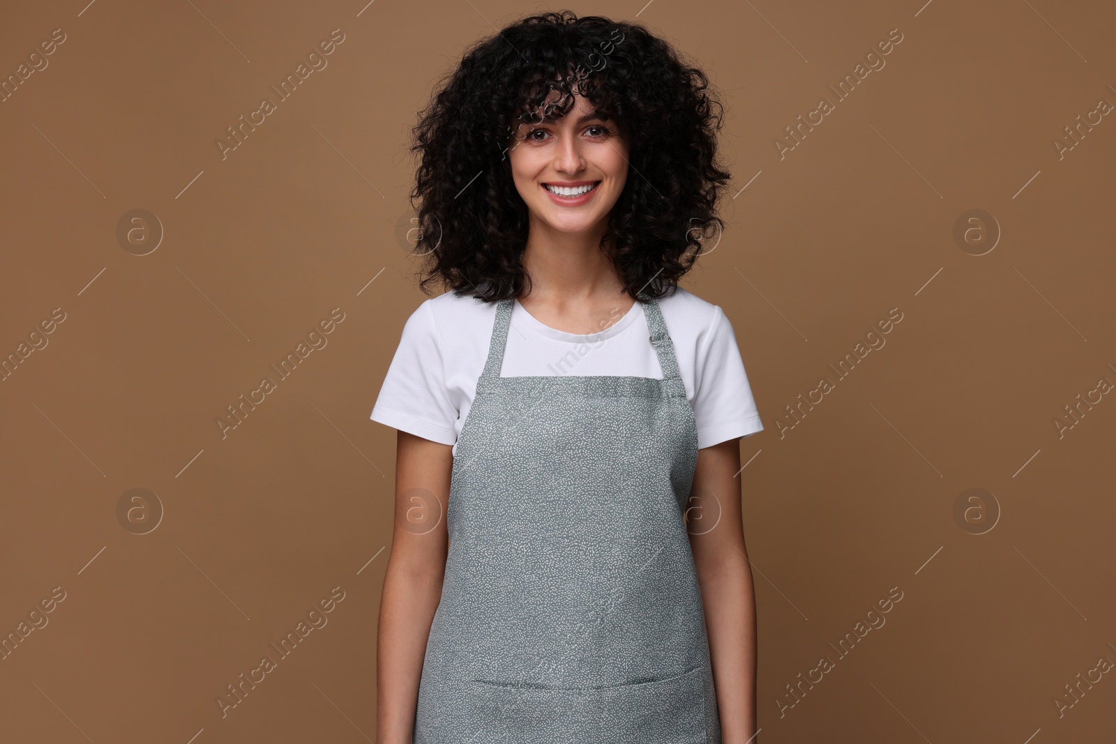 Photo of Happy woman wearing kitchen apron on brown background. Mockup for design