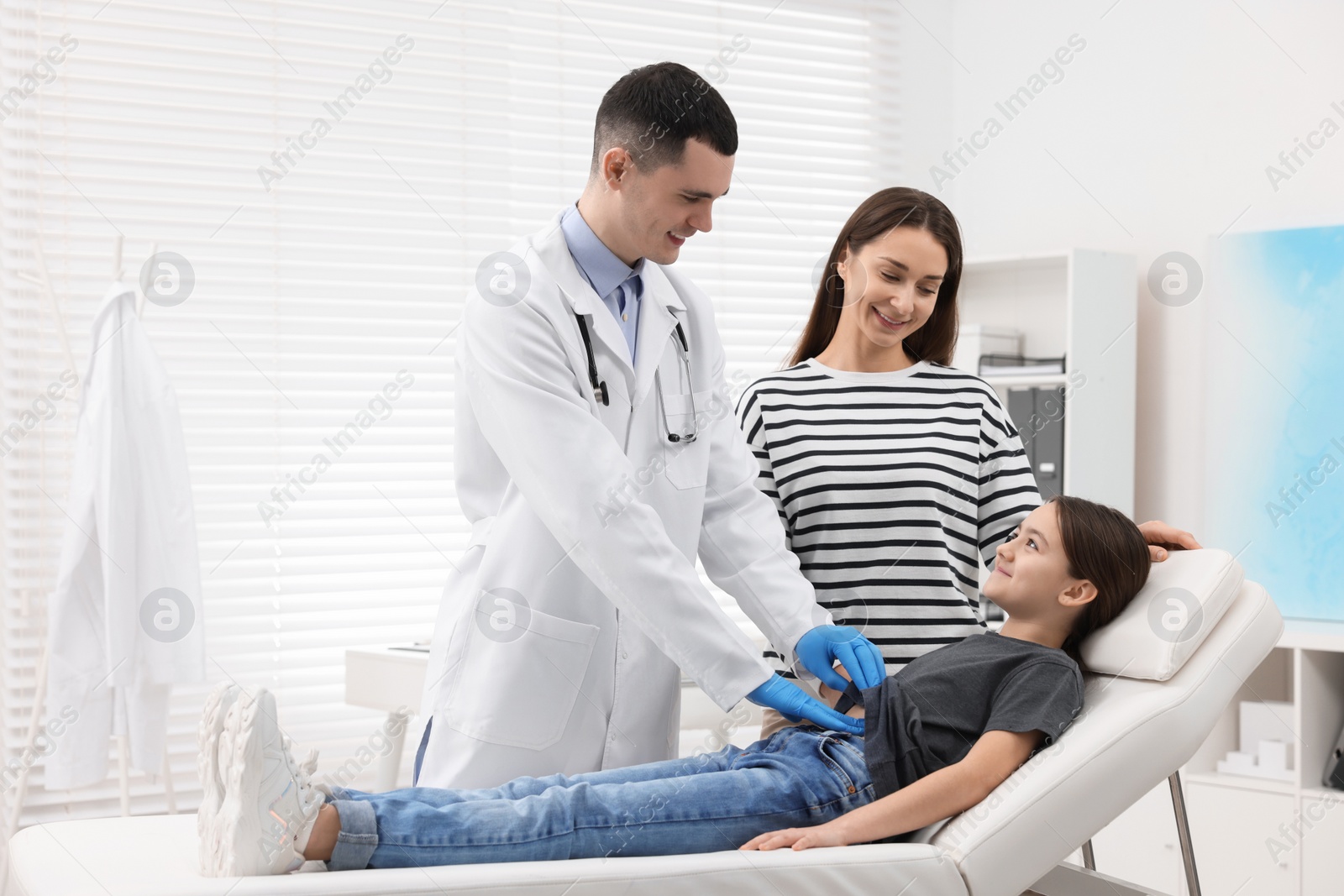 Photo of Gastroenterologist examining girl with stomach ache on couch in clinic