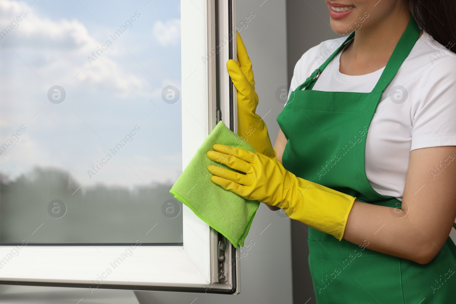Photo of Happy young woman cleaning window with rag indoors, closeup