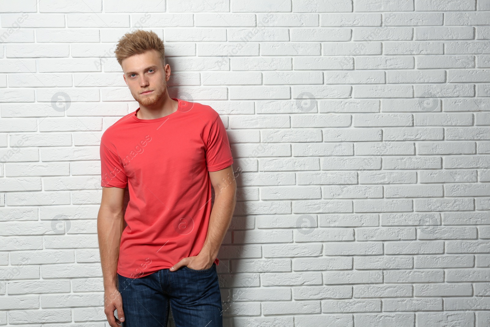 Photo of Young man wearing blank t-shirt near white brick wall. Mockup for design