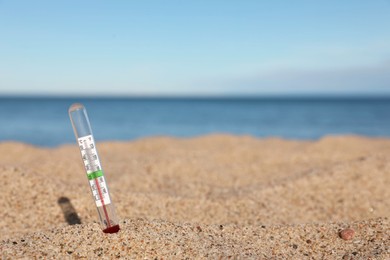 Photo of Weather thermometer in sand near sea, space for text
