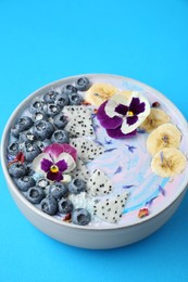 Delicious smoothie bowl with fresh fruits, blueberries and flowers on light blue background, closeup