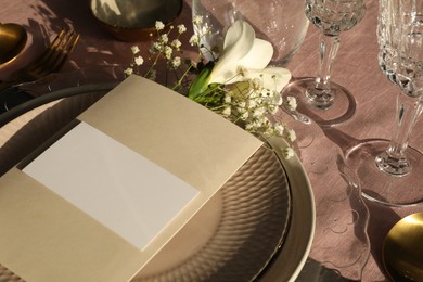 Stylish table setting. Dishes, glasses, blank card and floral decor, closeup