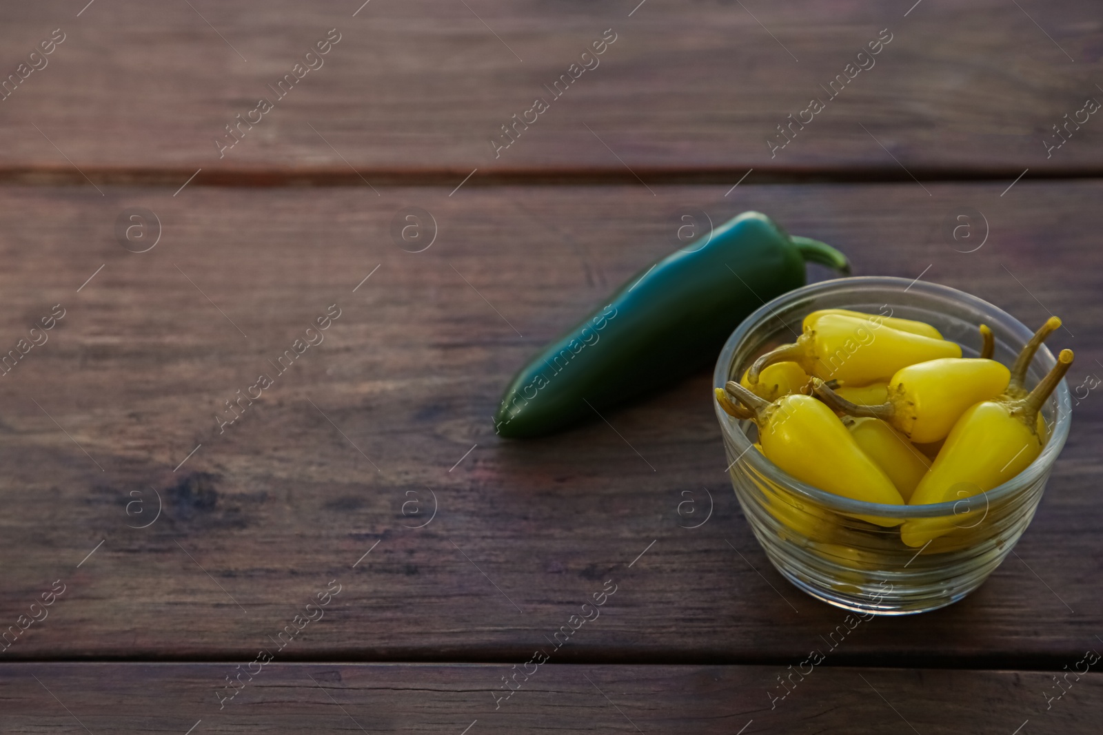 Photo of Fresh and pickled jalapeno peppers on wooden table. Space for text