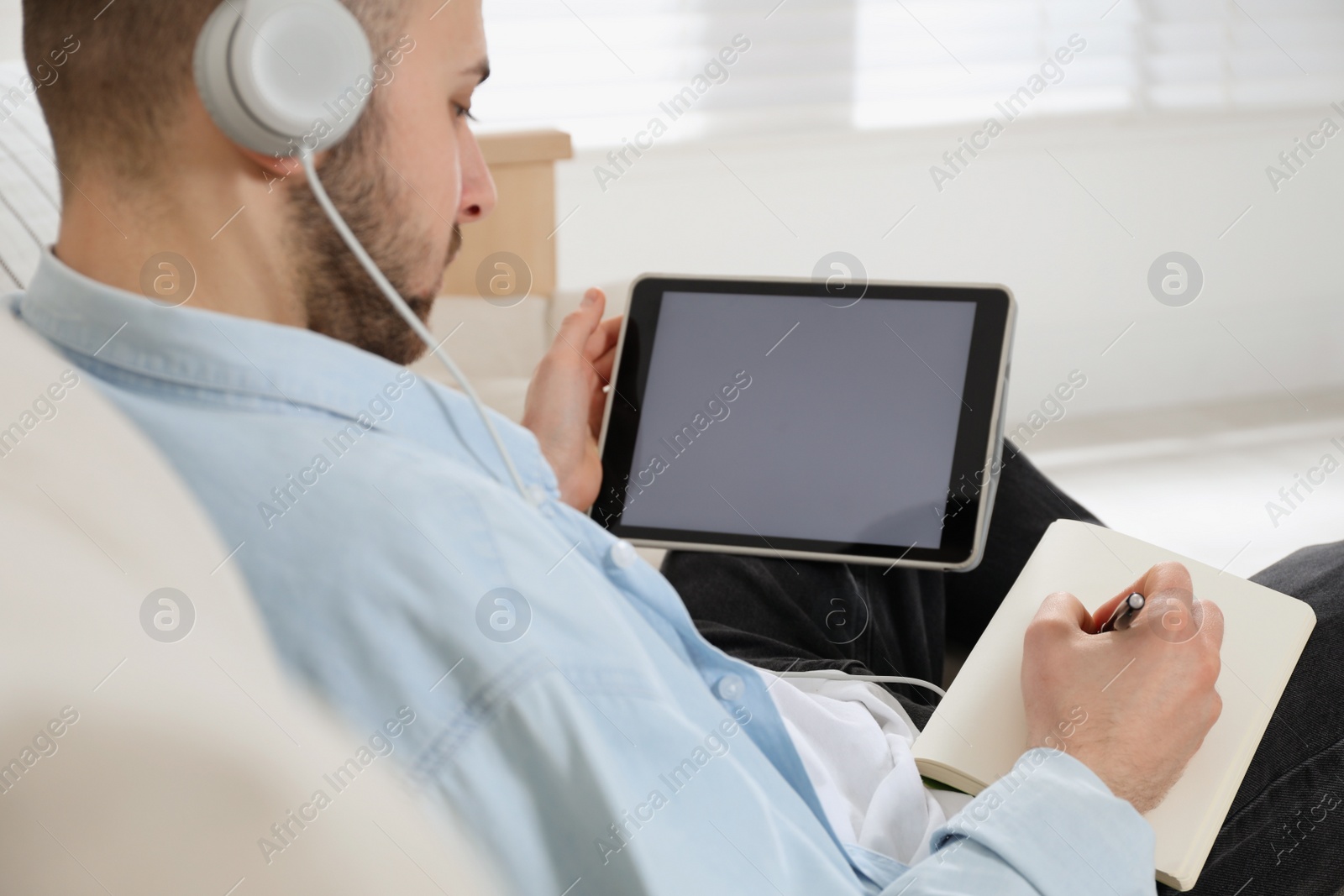 Photo of Young man with headphones using modern tablet for studying at home, closeup. Distance learning