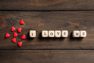 Phrase I Love Me made of small cubes and heart shaped sprinkles on wooden background, flat lay