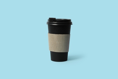 Takeaway paper coffee cup with cardboard sleeve on light blue background