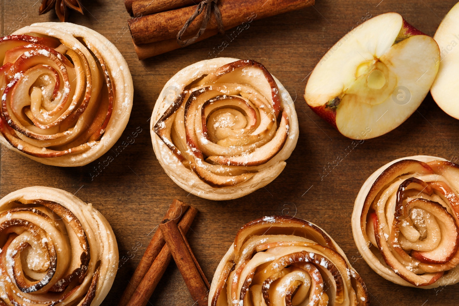 Photo of Freshly baked apple roses on wooden table, flat lay. Beautiful dessert