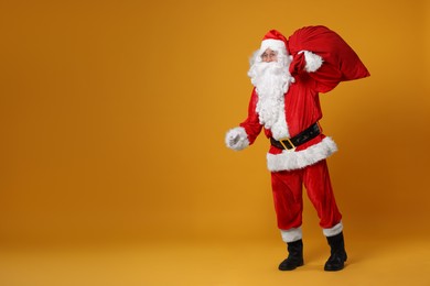 Photo of Santa Claus with bag of Christmas presents posing on orange background, space for text