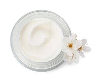Glass jar of face cream and flowers on white background, top view