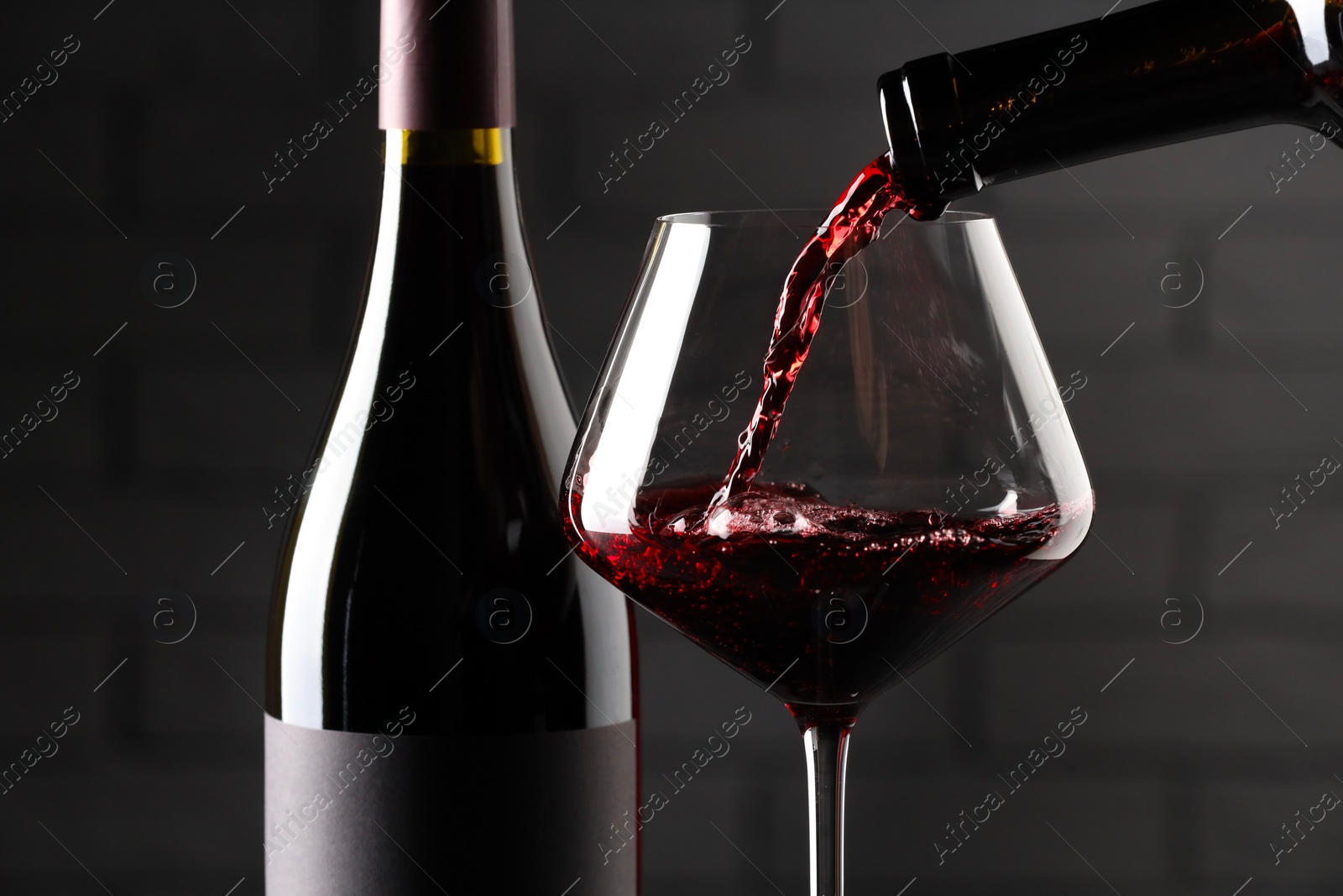 Photo of Pouring red wine into glass and bottles against brick wall background, closeup