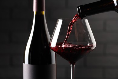 Photo of Pouring red wine into glass and bottles against brick wall background, closeup