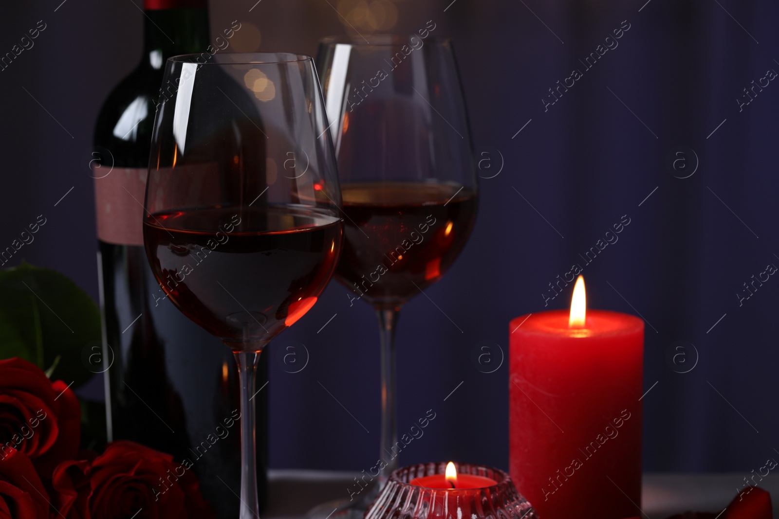 Photo of Glasses of red wine, rose flowers and burning candles against blurred background. Romantic atmosphere