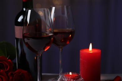 Glasses of red wine, rose flowers and burning candles against blurred background. Romantic atmosphere