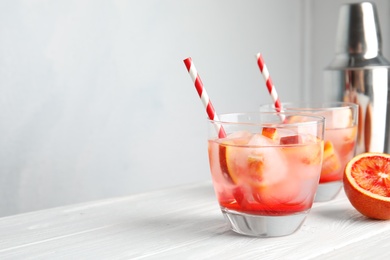 Glass of tropical cocktail with ice cubes on table against light background. Space for text