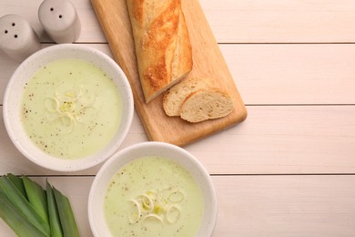 Bowls of tasty leek soup and bread on white wooden table, flat lay. Space for text