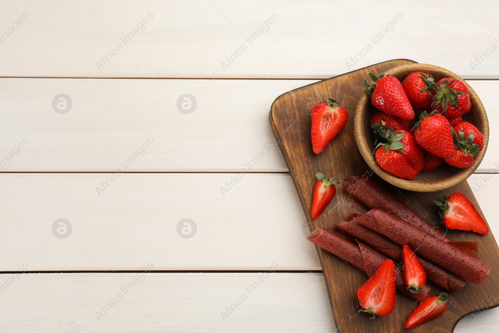 Photo of Delicious fruit leather rolls and strawberries on white wooden table, top view. Space for text