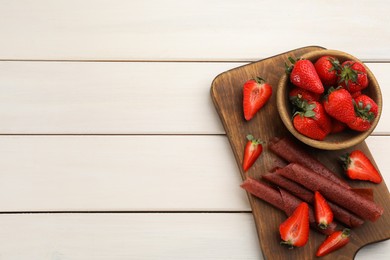 Photo of Delicious fruit leather rolls and strawberries on white wooden table, top view. Space for text