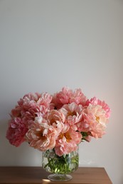Photo of Beautiful pink peonies in vase on table near white wall, space for text