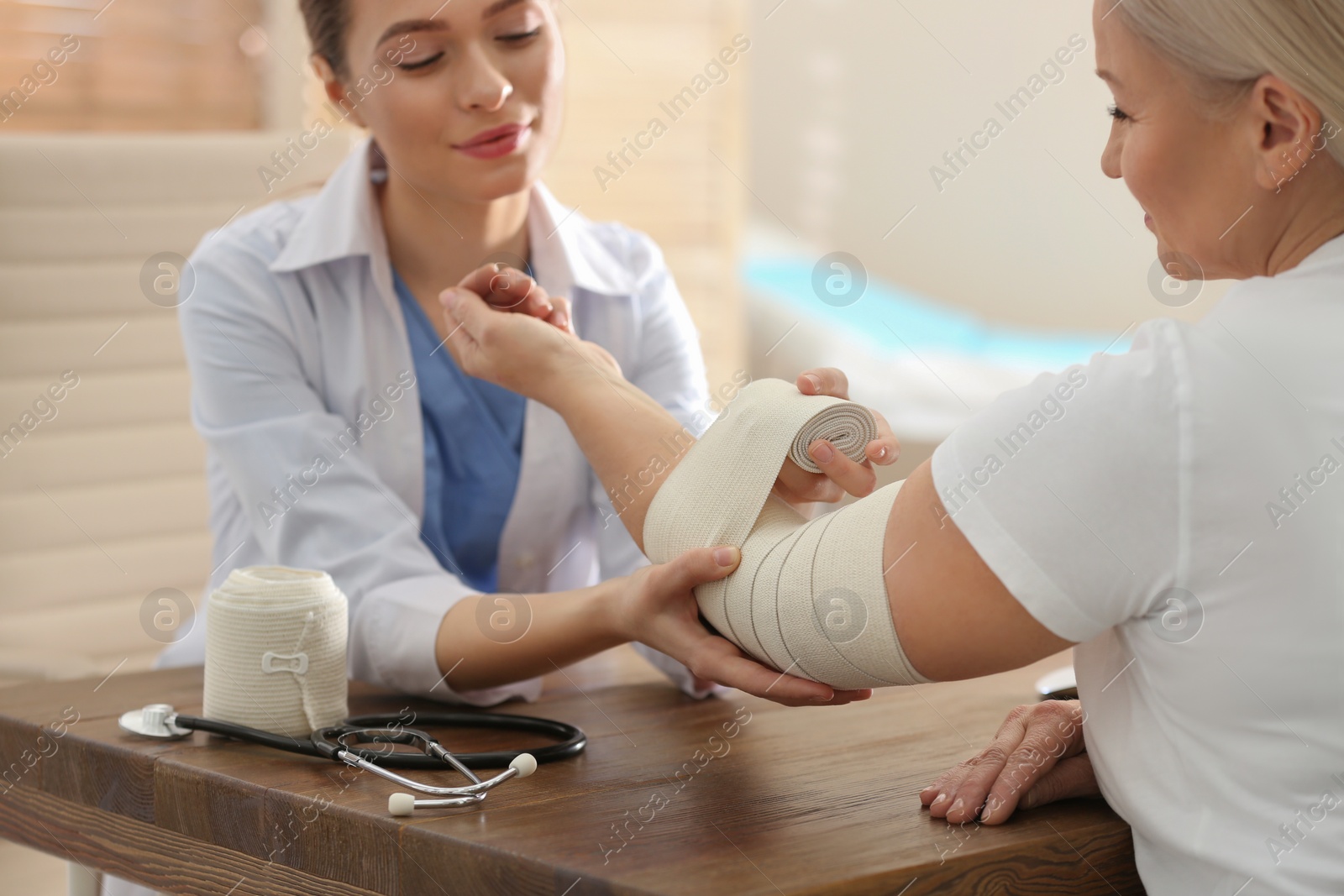 Photo of Female orthopedist applying bandage onto patient's elbow in clinic, closeup