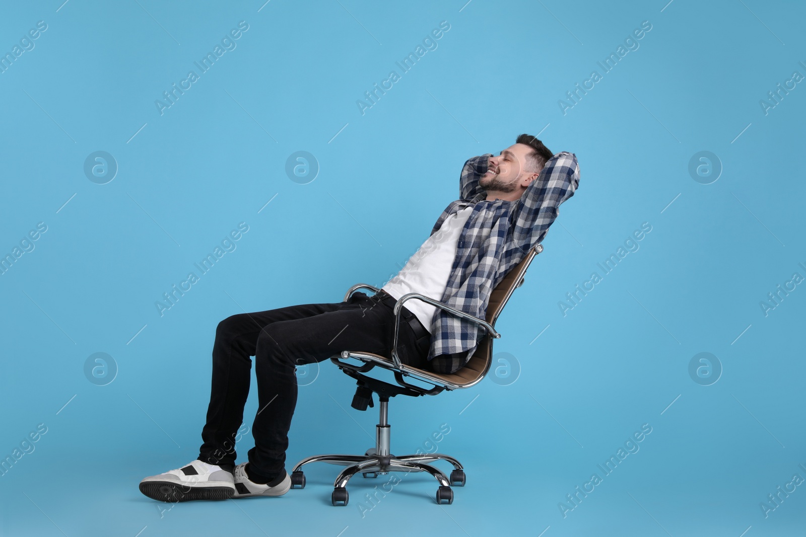 Photo of Handsome man relaxing in office chair on light blue background