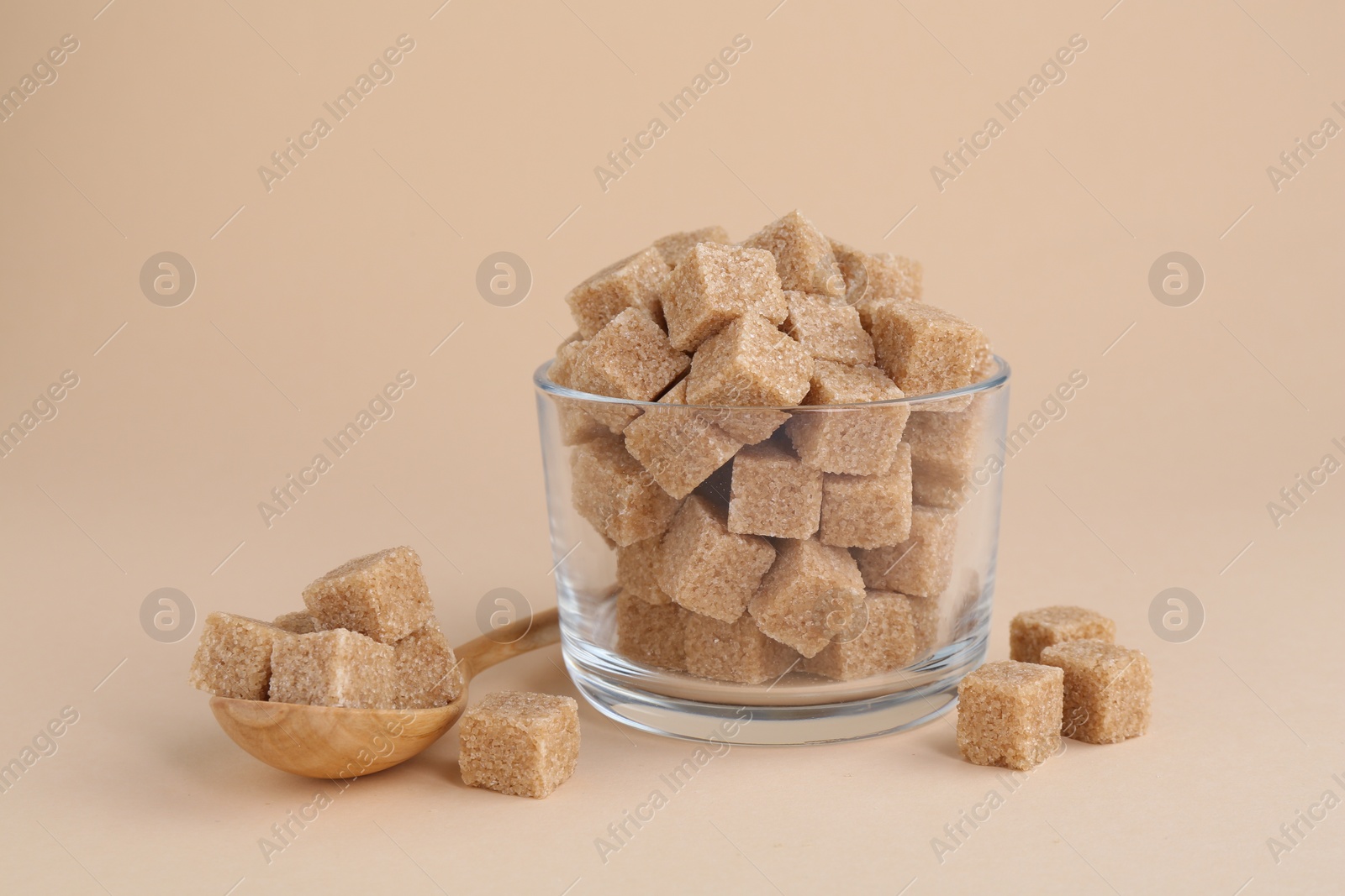 Photo of Brown sugar cubes in glass and spoon on beige background, closeup