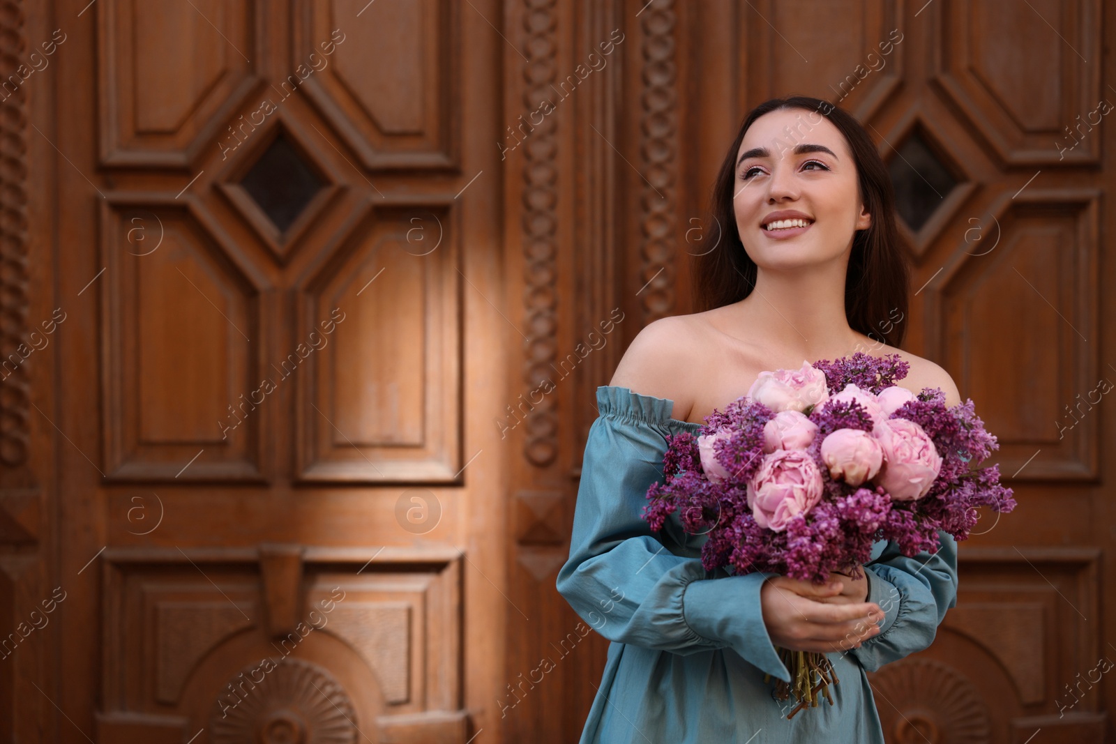 Photo of Beautiful woman with bouquet of spring flowers near wooden doors outdoors, space for text