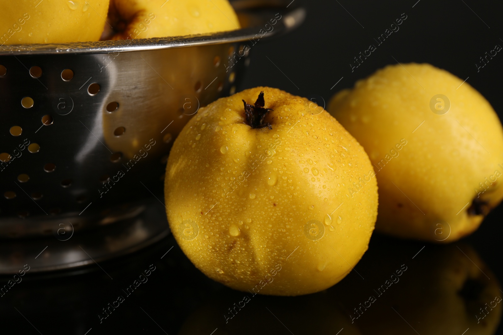 Photo of Tasty ripe quinces and metal colander on black mirror surface, closeup