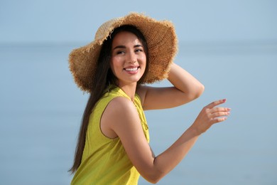 Photo of Beautiful young woman wearing straw hat on blurred background. Stylish headdress