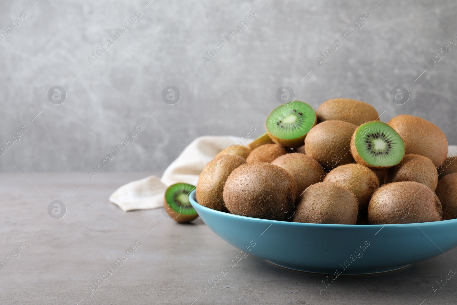 Photo of Fresh ripe kiwis in bowl on light grey table, space for text