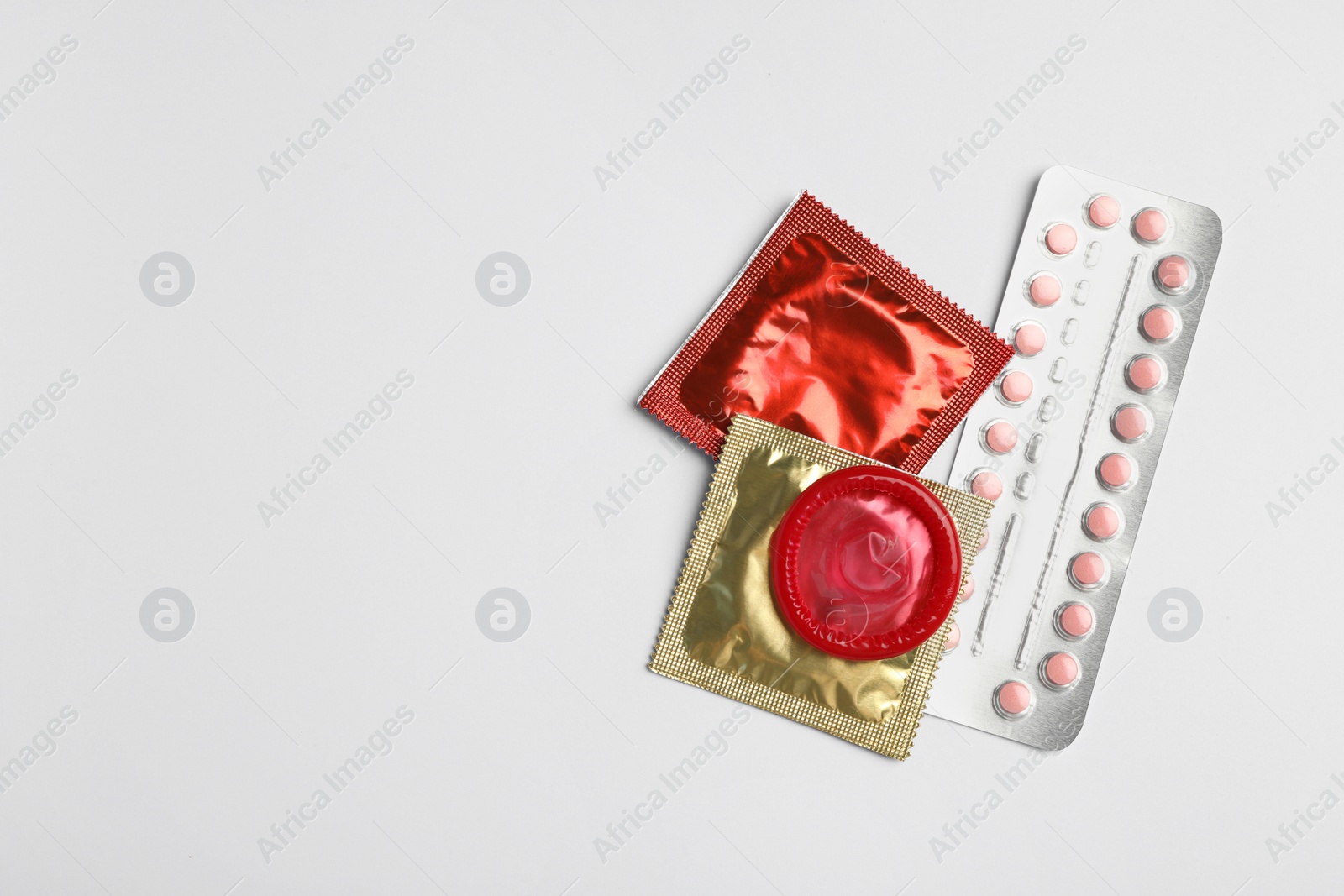 Photo of Condoms and birth control pills on light grey background, flat lay with space for text. Safe sex concept