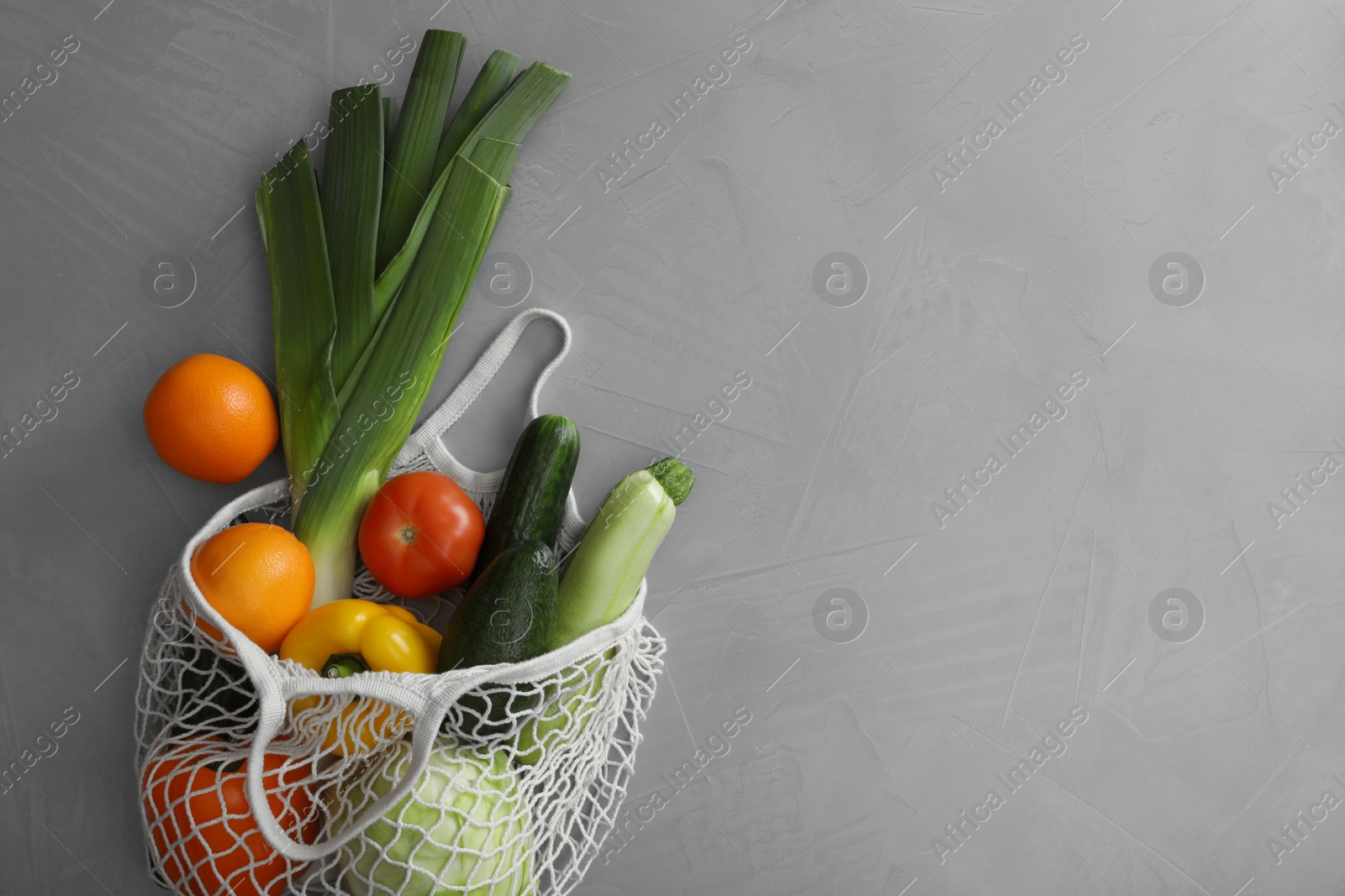 Photo of Net bag with fruits and vegetables on light grey table, flat lay. Space for text