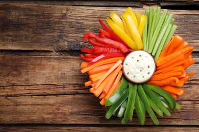 Photo of Different vegetables cut in sticks and dip sauce on wooden table, top view. Space for text