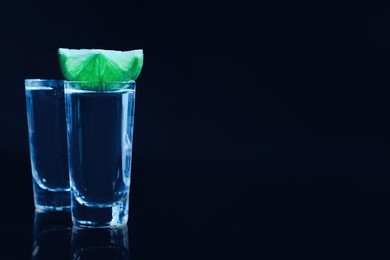 Photo of Shot glasses of vodka with lime slice on dark background, space for text