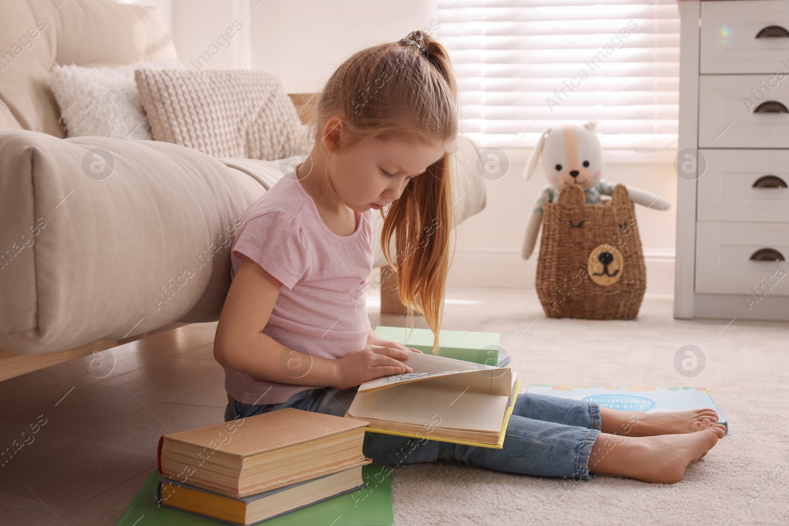 Photo of Cute little girl reading book on floor at home