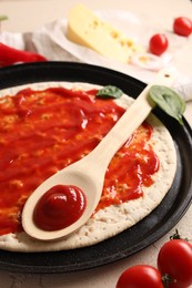 Pizza base smeared with sauce and tomatoes on light textured table, closeup