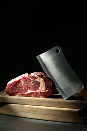 Photo of Piece of raw beef meat and knife on grey table against black background