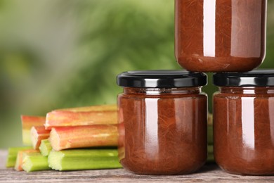 Jars of tasty rhubarb jam and stalks on wooden table, closeup