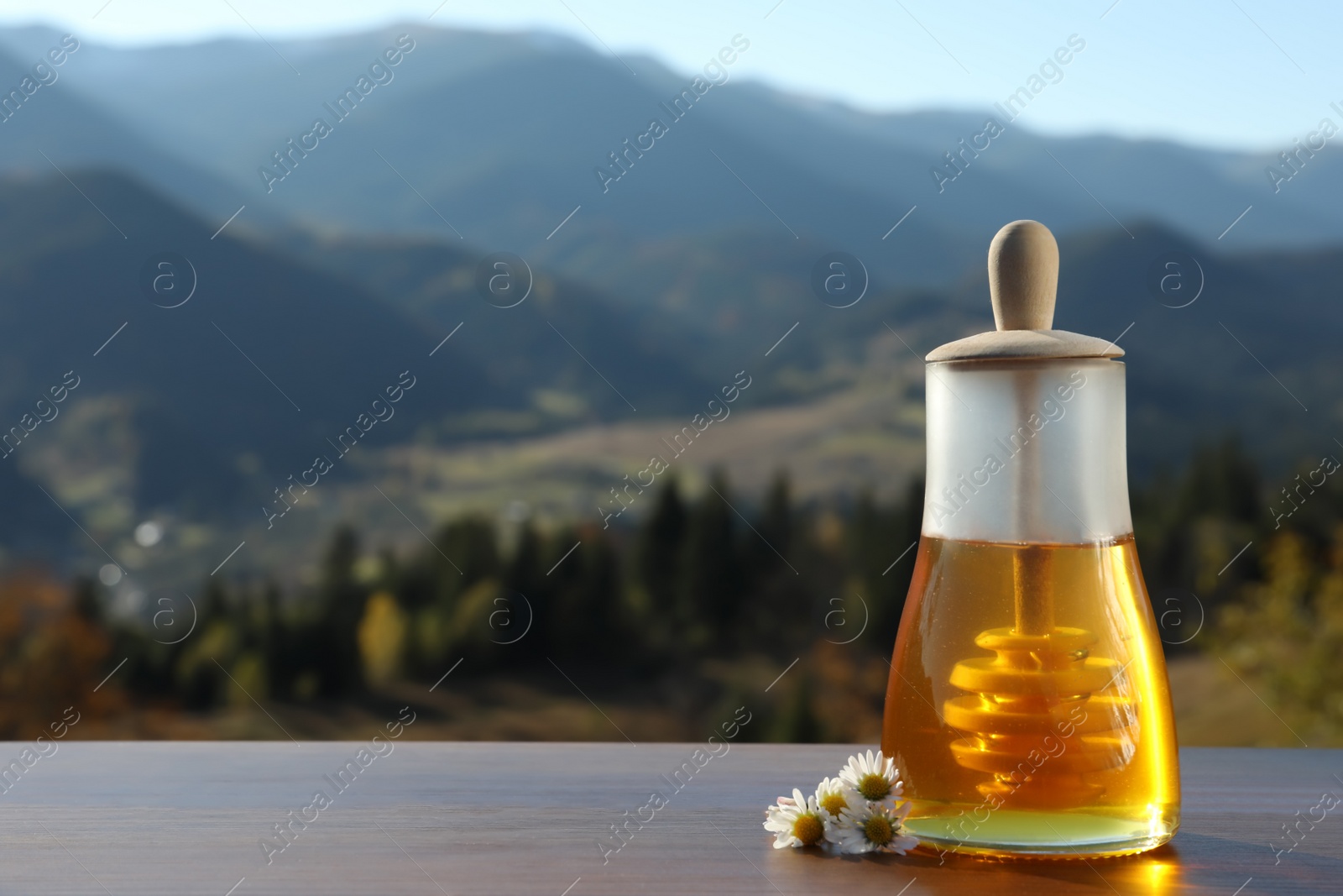 Photo of Fresh aromatic honey and chamomile flowers on wooden table against mountain landscape. Space for text