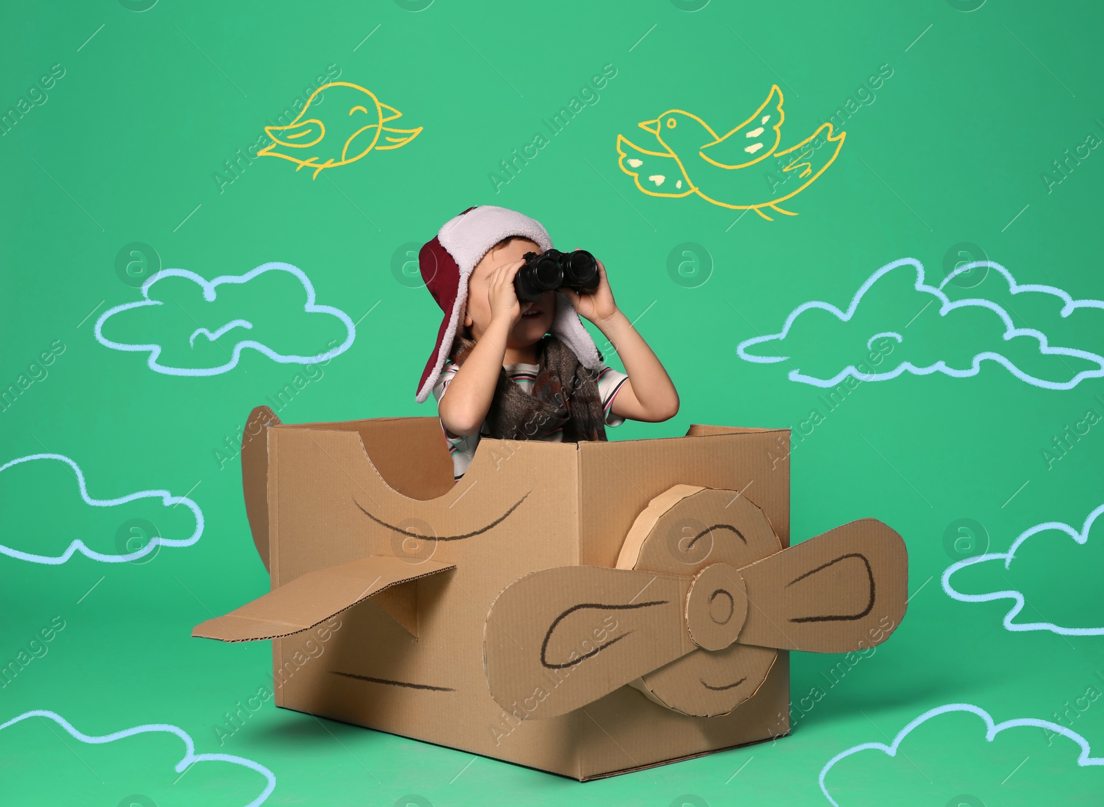 Image of Cute little child playing in cardboard airplane on green background with illustrations