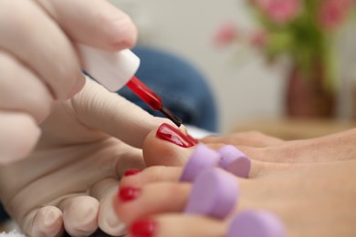Photo of Pedicurist painting client`s toenails with red polish in beauty salon, closeup