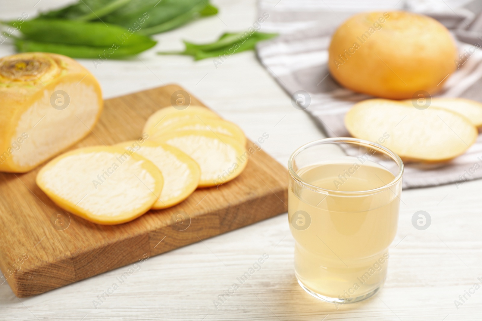 Photo of Glass of fresh natural turnip juice and cut root on white wooden table, space for text