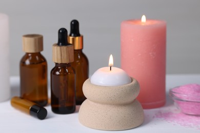 Different aromatherapy products and burning candles on white table, closeup