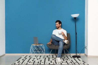 Photo of Man looking at laptop and holding coffee cup in stylish room interior, space for text